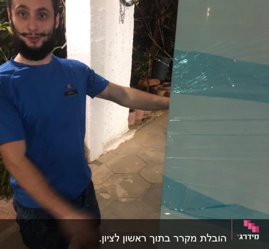 אדם בחולצה כחולה מחזיק חפץ עטוף בניילון